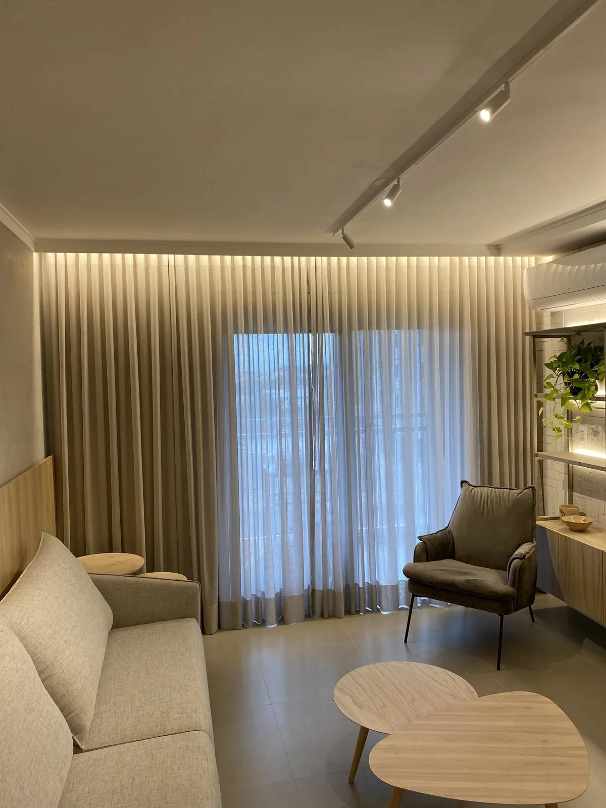 Living com cortinas de tecido e iluminação indireta no cortineiro
