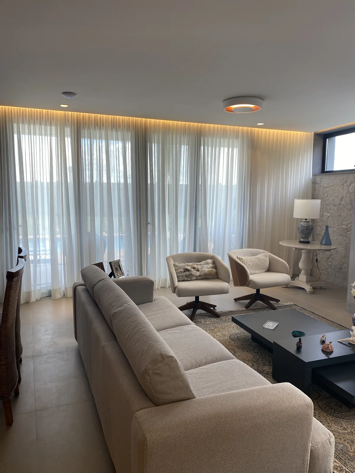 Sala integrada com cortina de tecido leve ocupando uma parede envidraçada